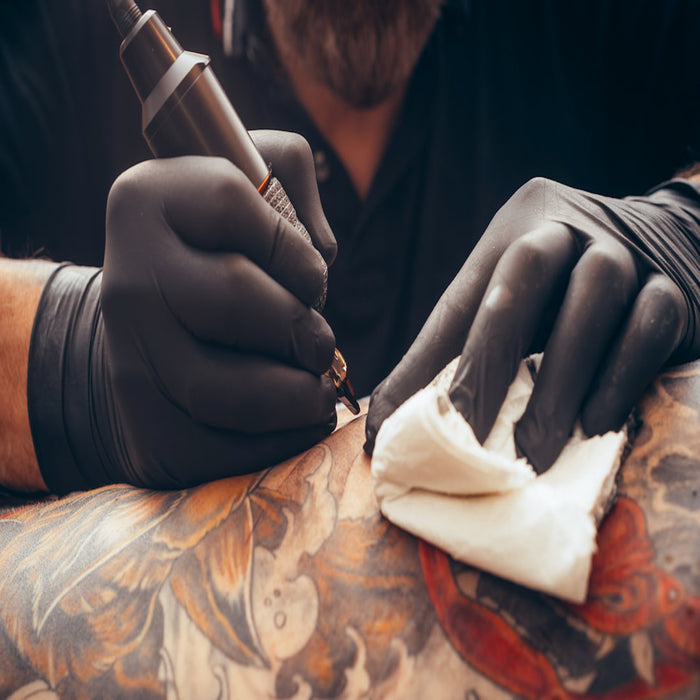 Tattoo Artist using Advance IF 51 Black 5 Mil Nitrile Examination Gloves to draw on his Client's  Arm